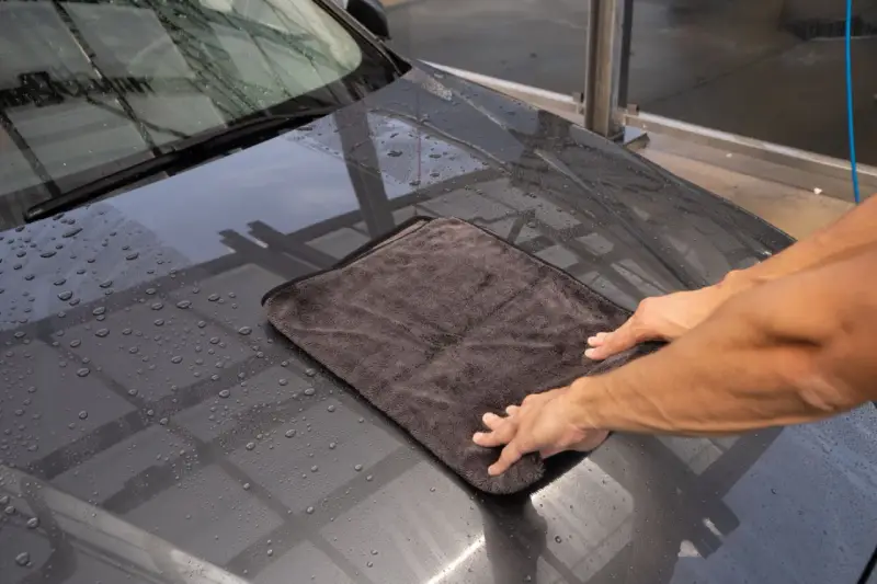 Hände trocknen das nasse Auto mit einem weichen auto trockentuch.