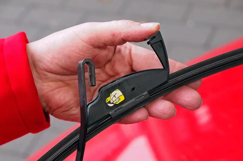 Hand wechselt Scheibenwischer an einem VW. Der Haken des Wischerarms wird in die Halterung eingeführt.