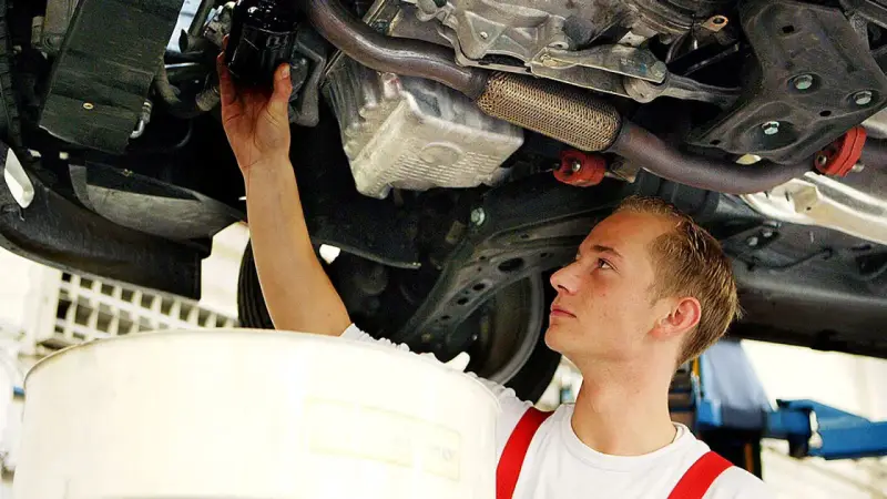 Ein junger Mechaniker bei einer Arbeitsstunde in der Kfz Werkstatt wechselt den Ölfilter unter einem Auto.