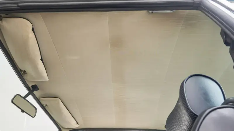 Der Dachhimmel kleben ist eine Kunst. Hier sieht man den hellen, gemusterten Dachhimmel eines Autos, mit Sonnenblenden und Rückspiegel.