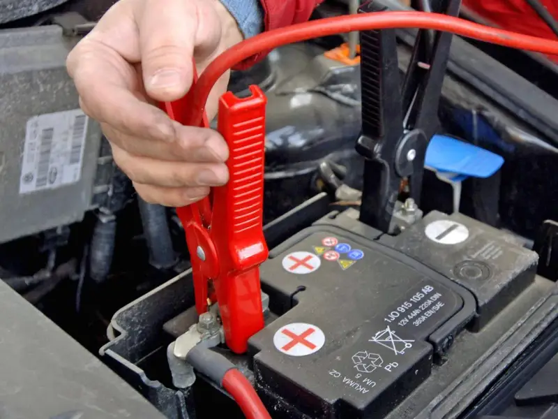 Starthilfe Auto: Rote Klemme wird am Pluspol der Batterie befestigt. Die richtige Reihenfolge ist entscheidend für die Sicherheit.